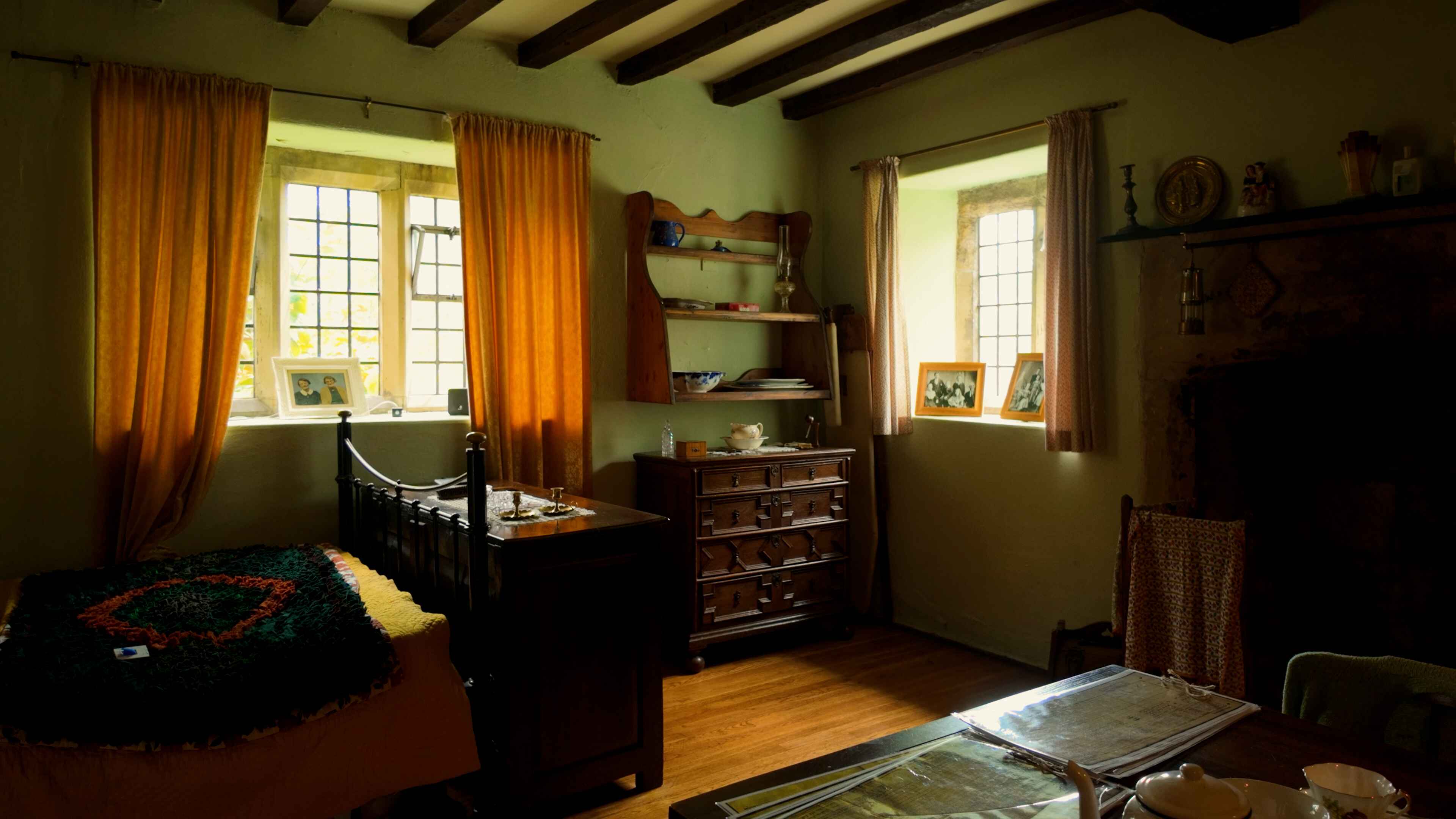 A well-furnished bedroom with a bed, dresser, table, and two windows providing a view outside
