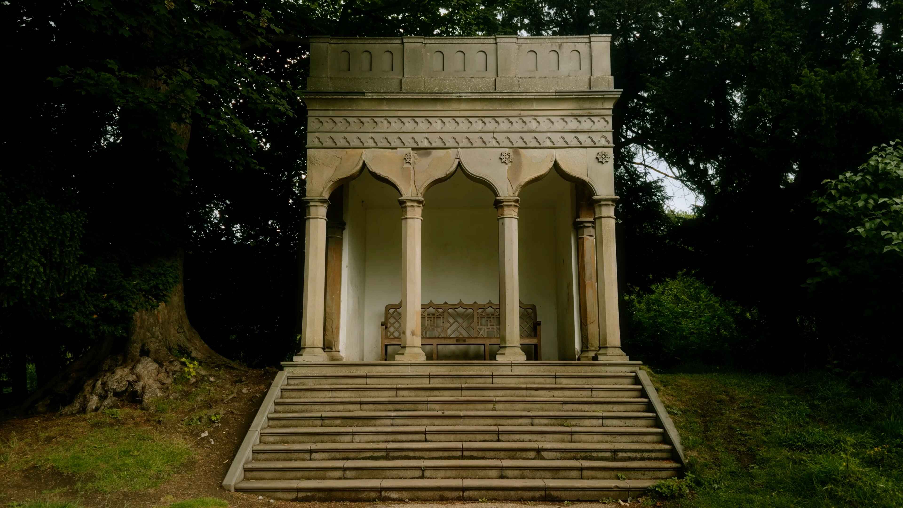 A gothic style outhouse building with stairs leading up to a seating bench inside it