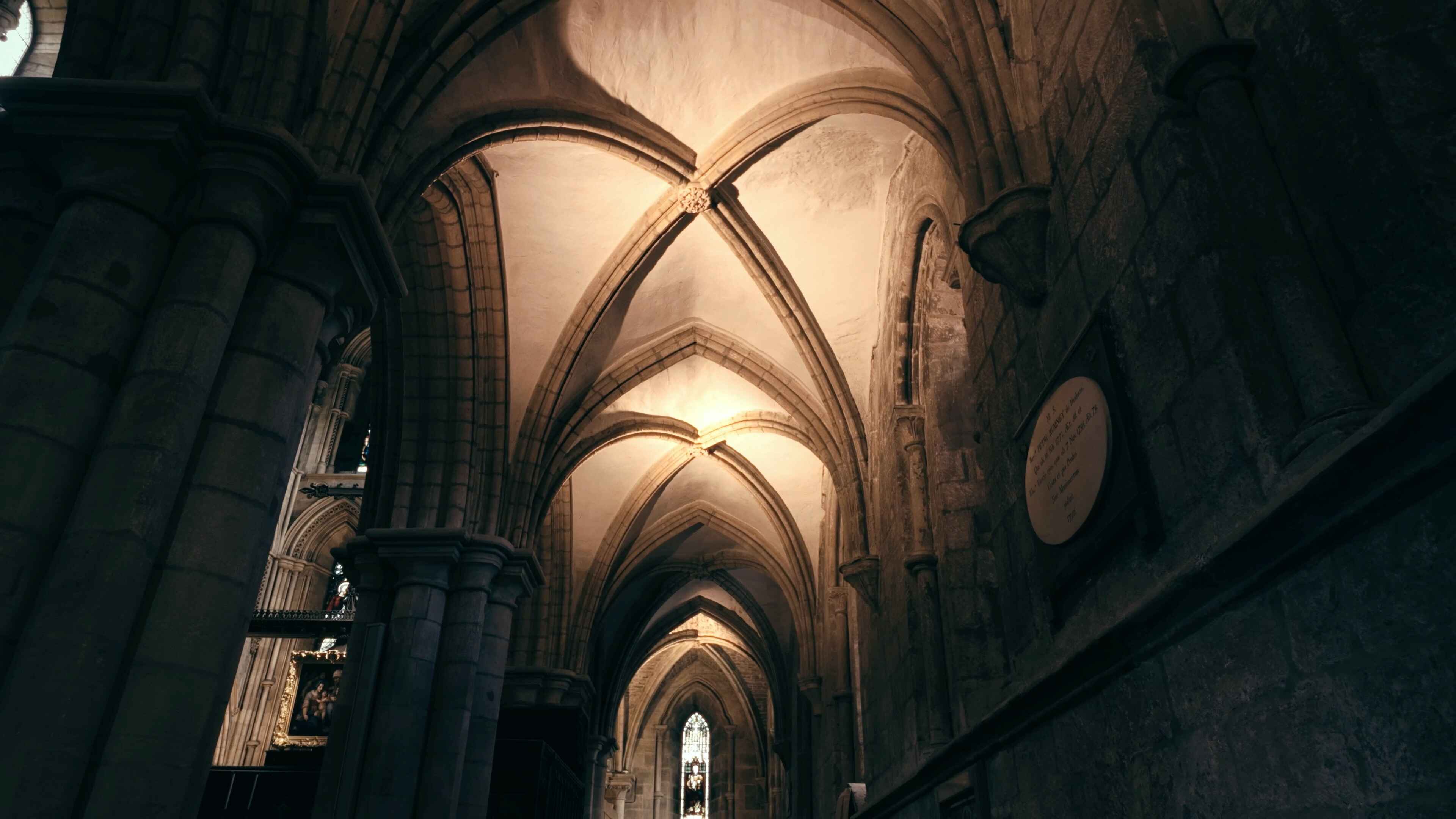 A long archway with a stained glass window in the distance and a painting to the left