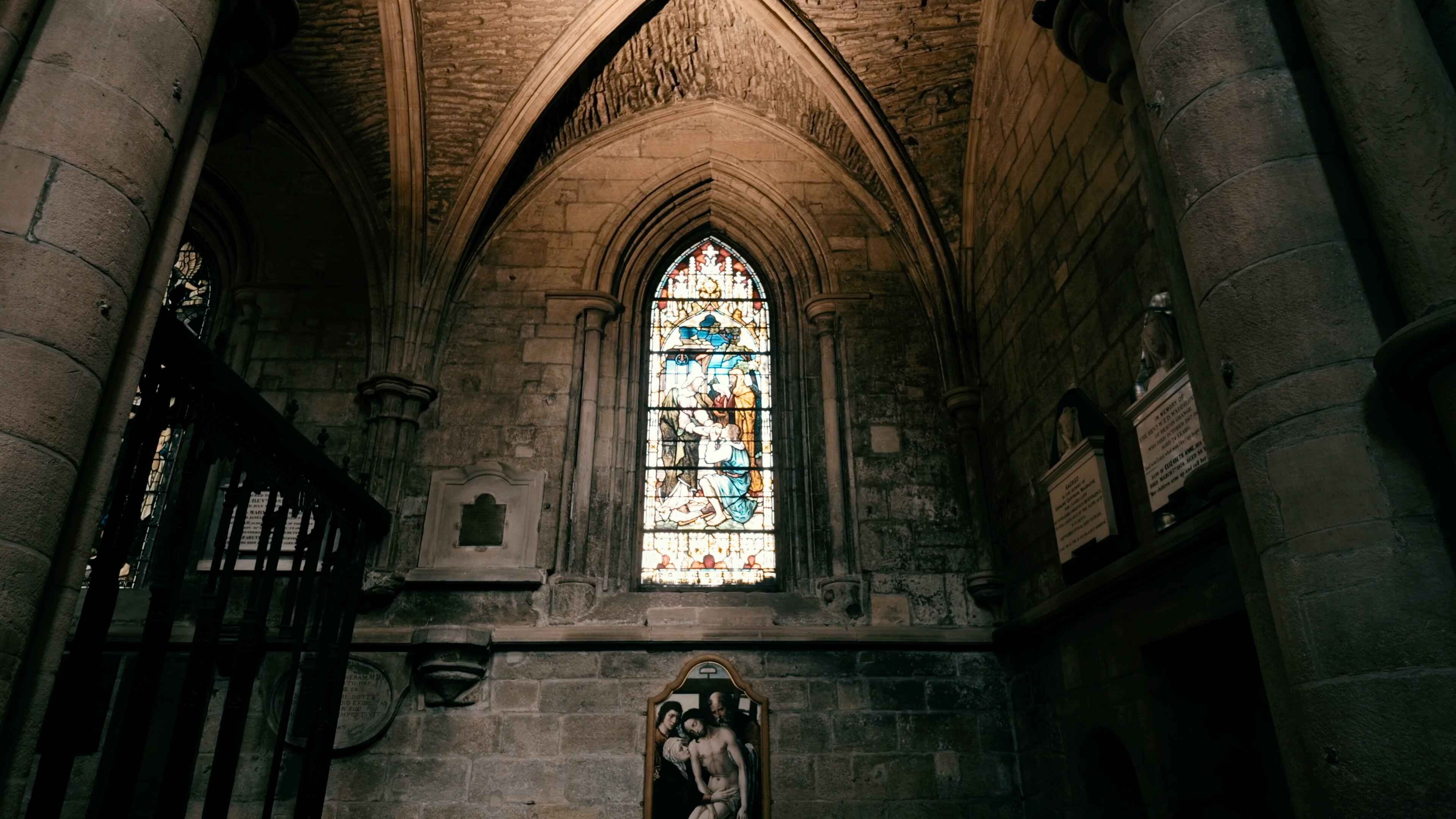 A stained glass window under an archway with a painting of Jesus Christ underneath