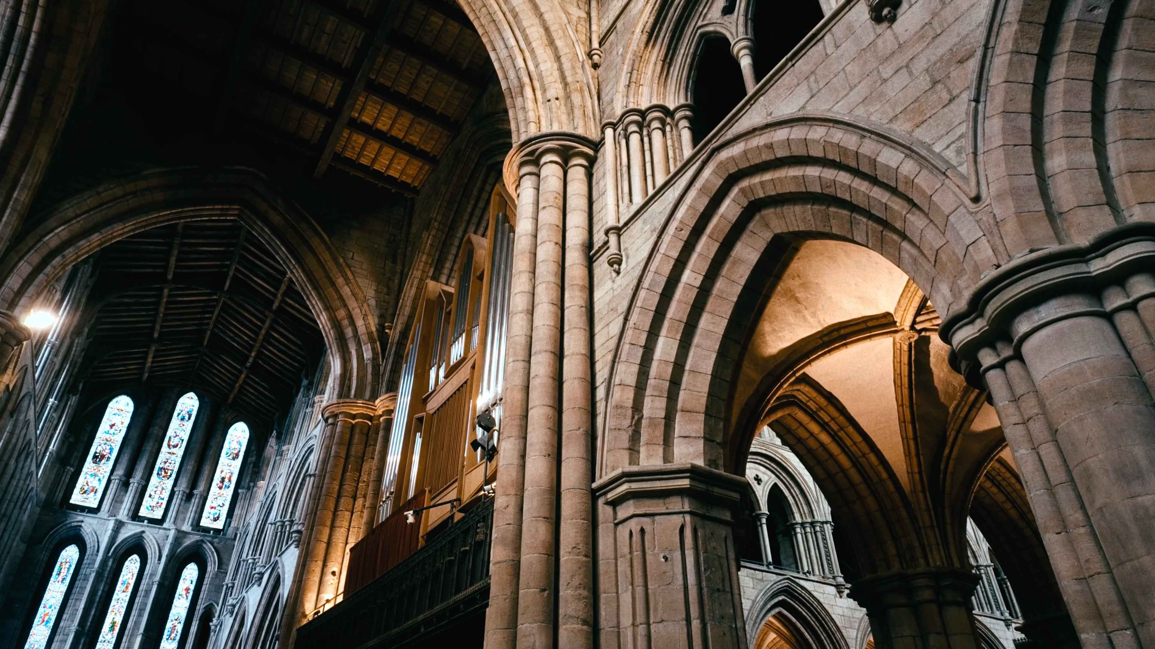 A stained glass window in the distance and stone archways all in an abbey