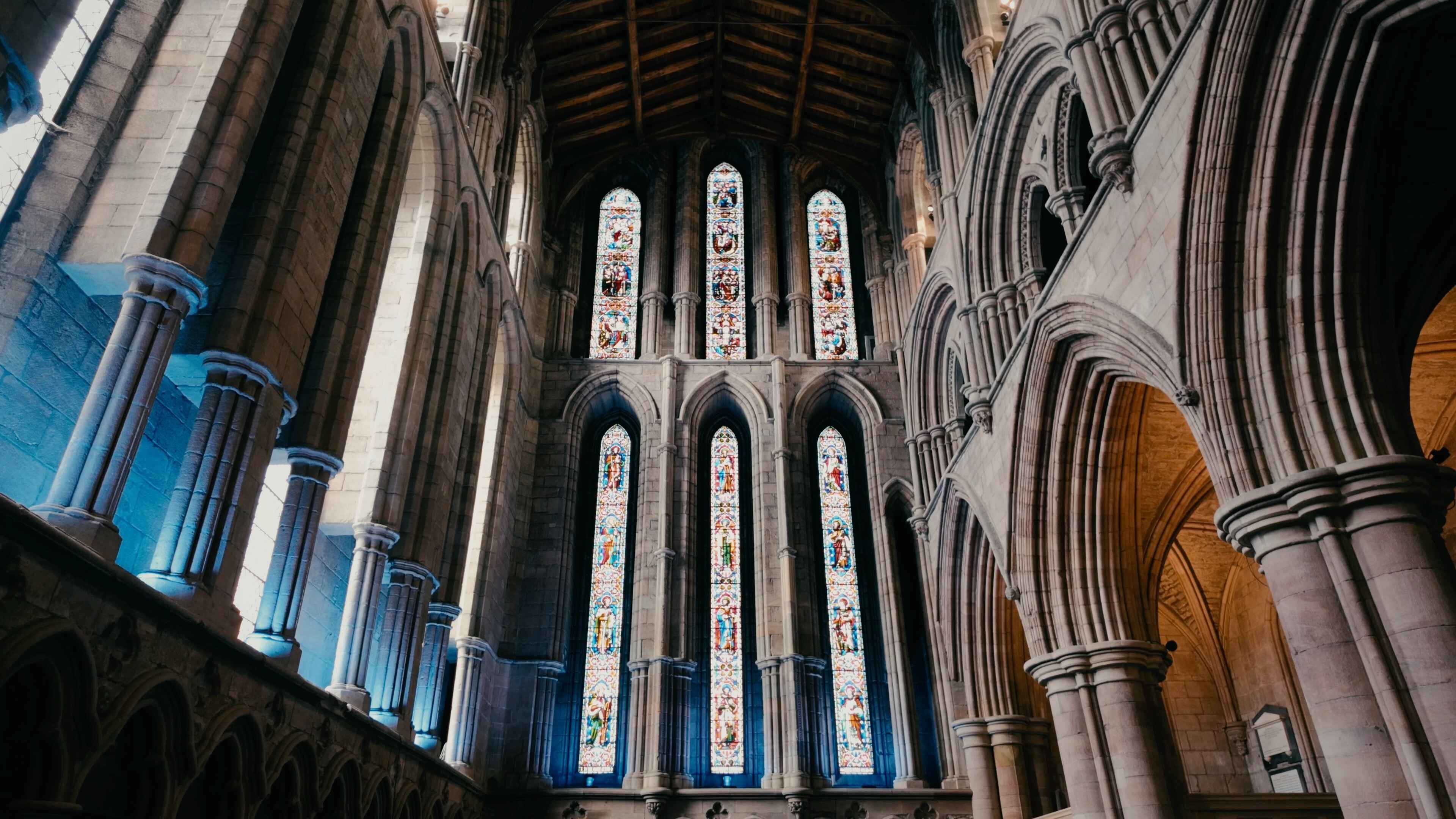 A series of slim stained glass windows rising to the ceiling in a stone-built abbey