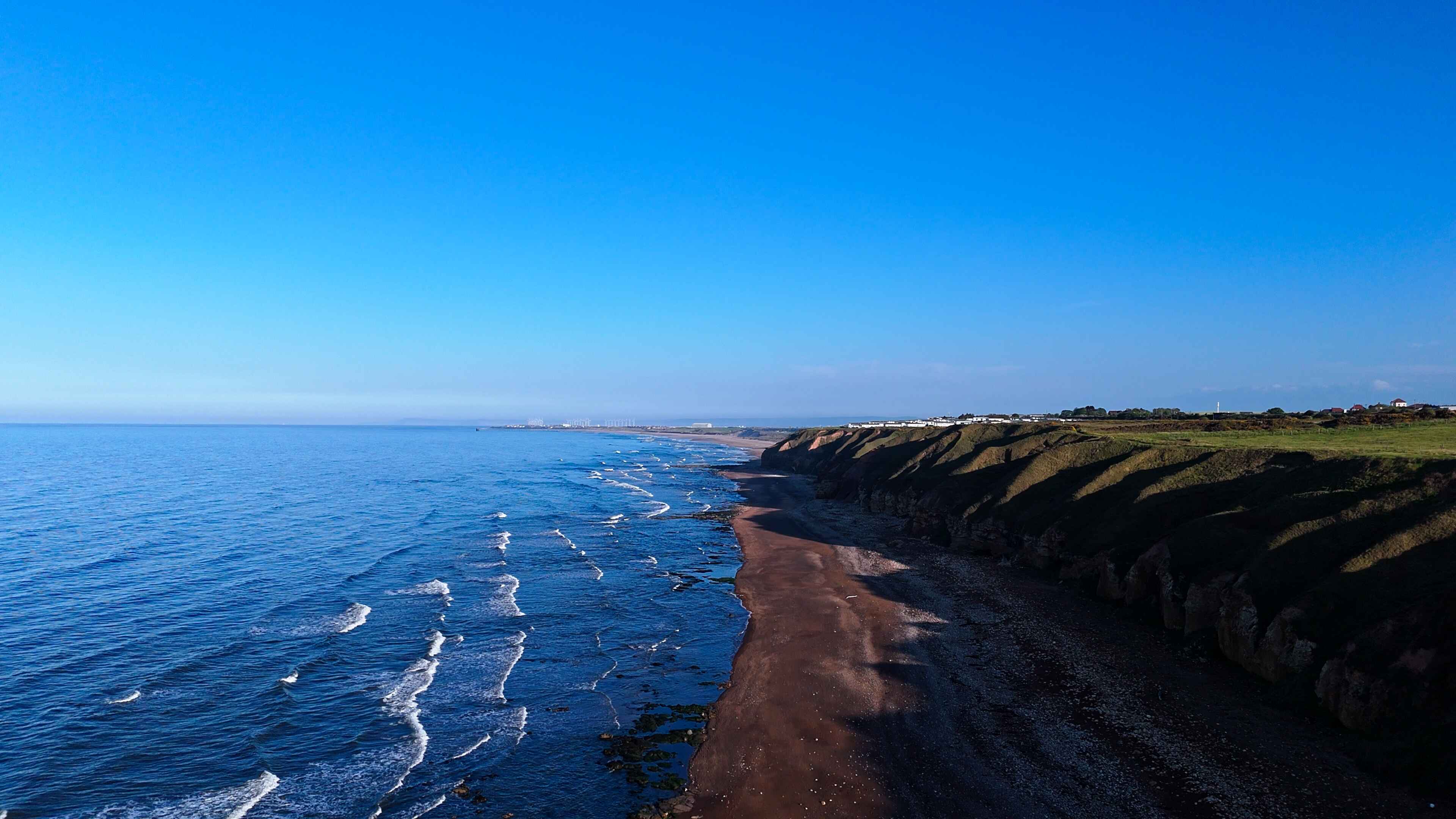 Striking blue water to the left laps over dark-shaded sands under a blue sky