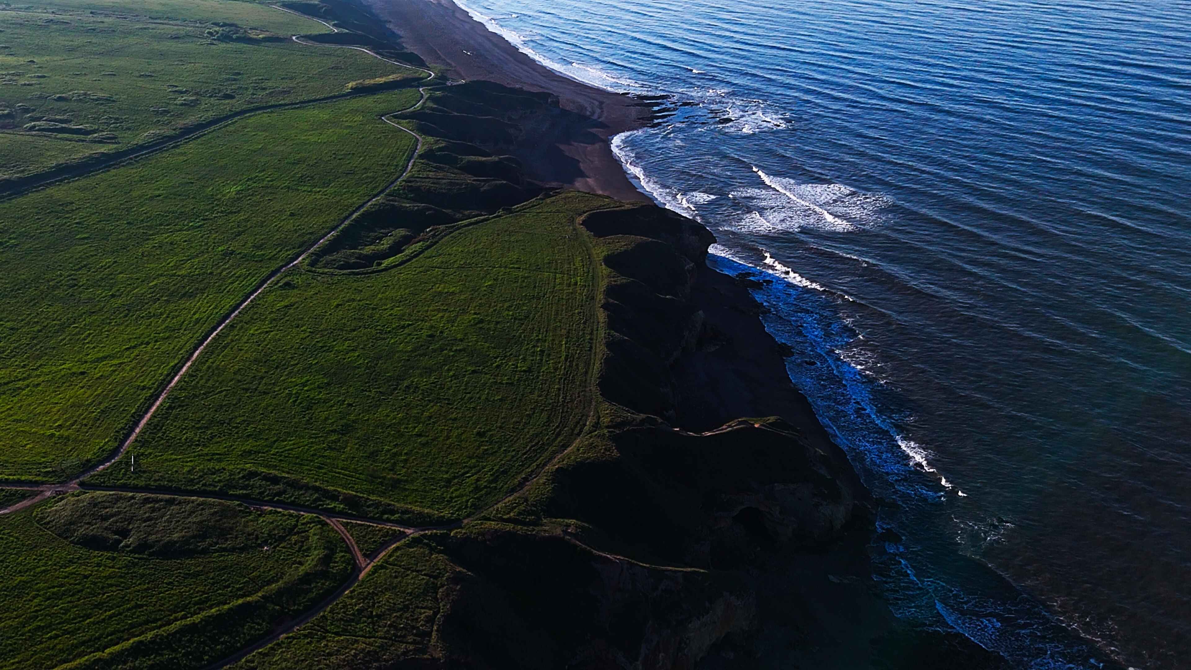 Lush green cliffs to the left overlook a large body of beach-front water