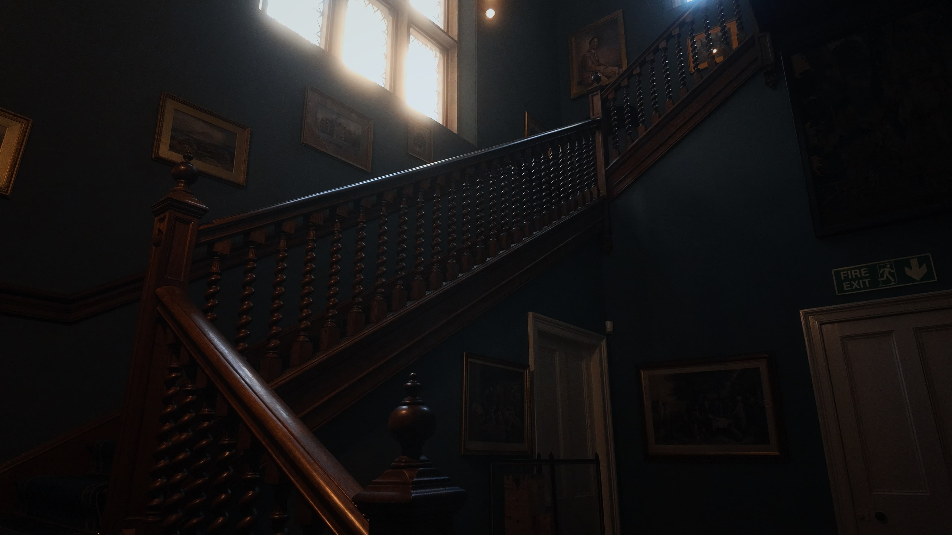 A wooden staircase with a deep blue wall and several paintings going upwards