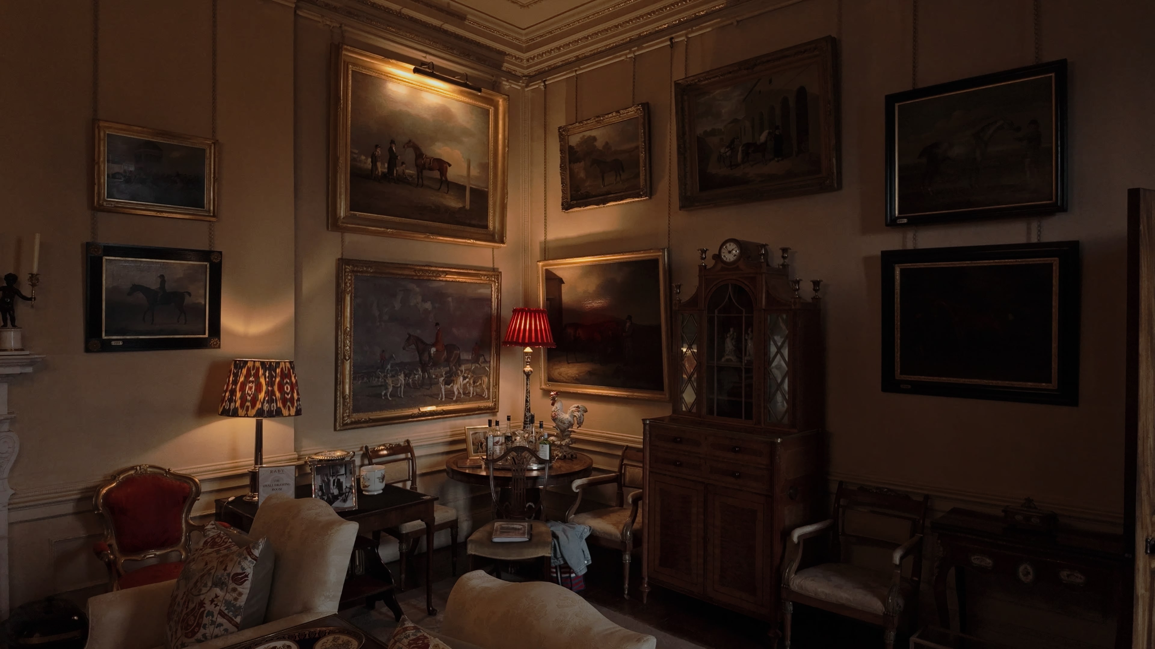 A corner of a resting room with a cabinet, chairs, tables and several paintings