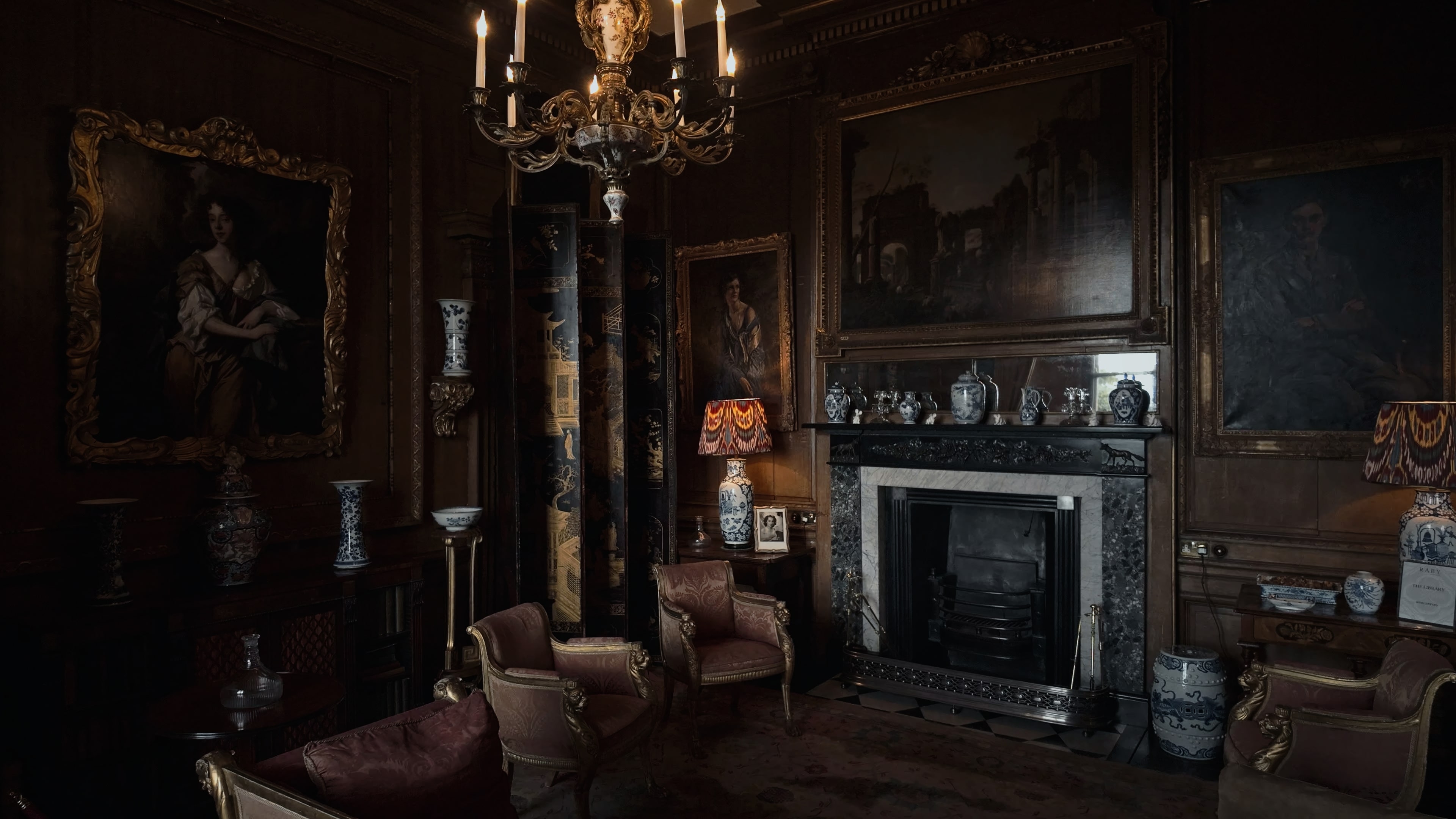 The corner of an opulent interior with two chairs, a series of paintings and a chandelier