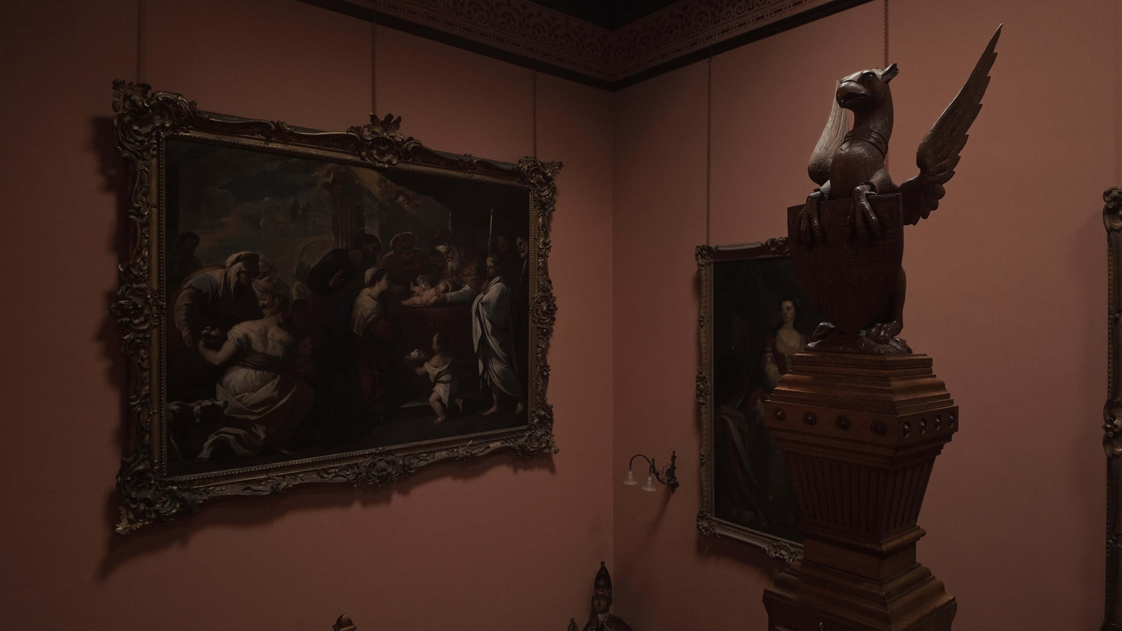 An ornate wooden sculpture of an animal atop a staircase with a painting on the wall