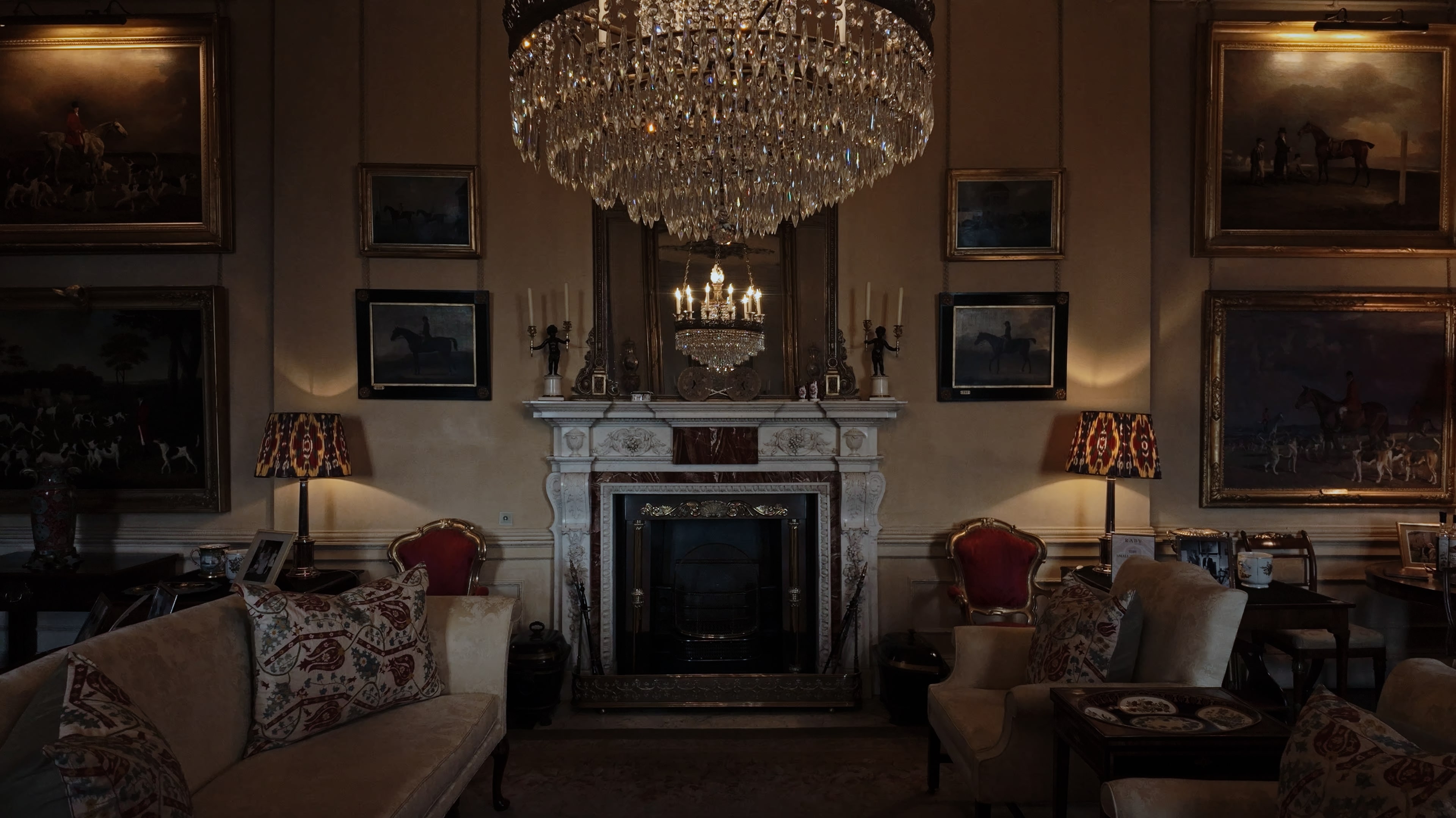 A fireplace with a large chandelier overhead, red-lined chairs and white couches
