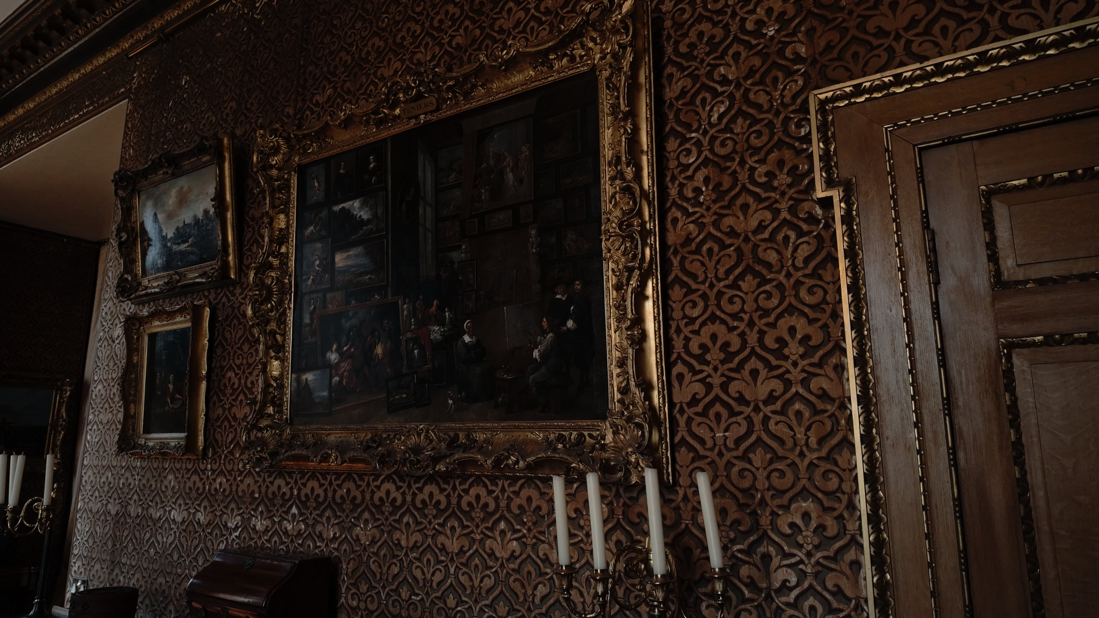 A close up of a wall-mounted painting and an unlit candlebraum