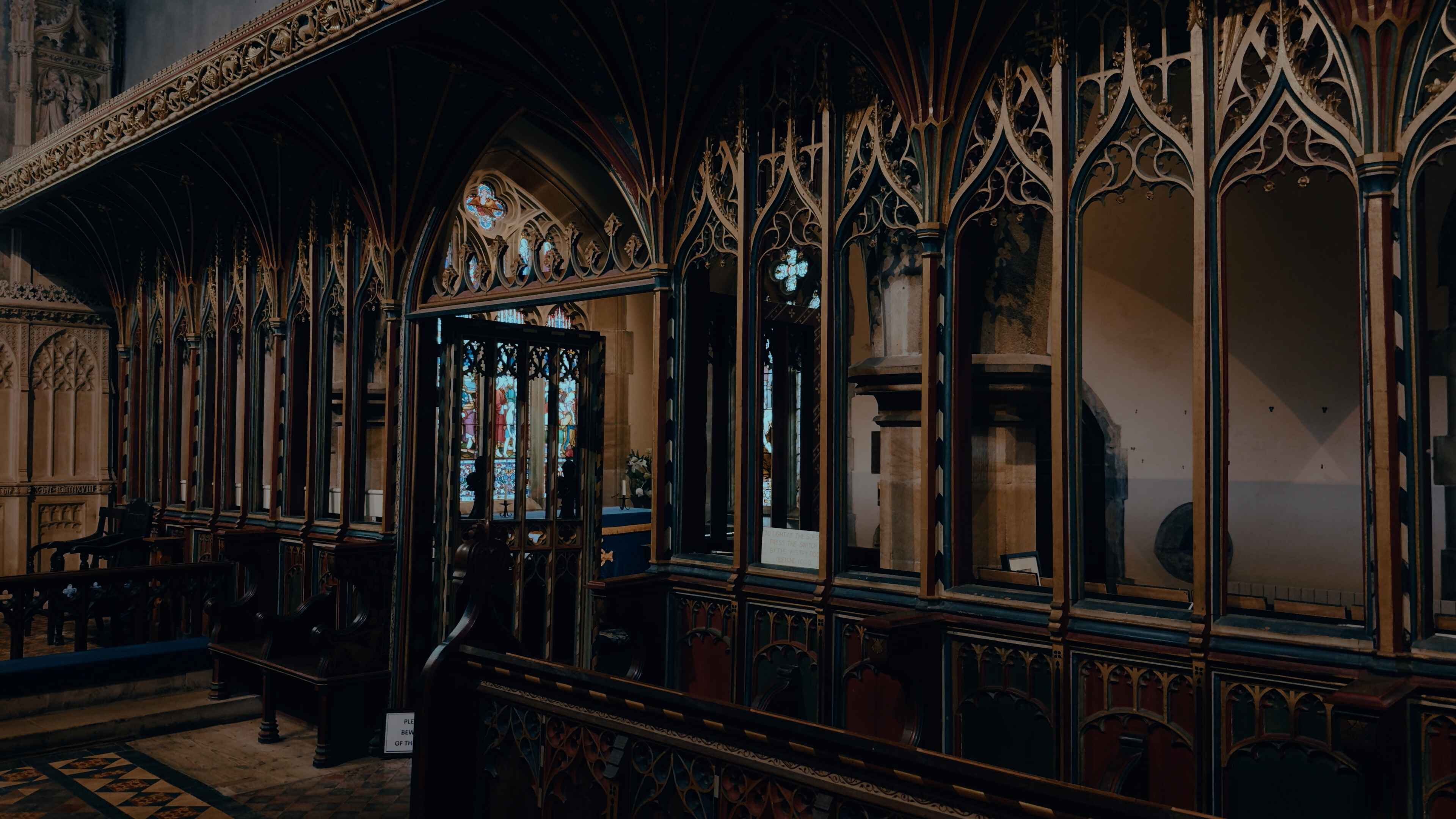 A rood screen in front of church pews, with stained-glass windows behind