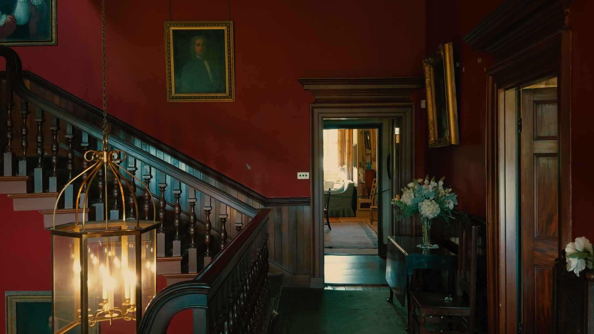 The interior of a grand home, with a chandelier, red walls and paintings