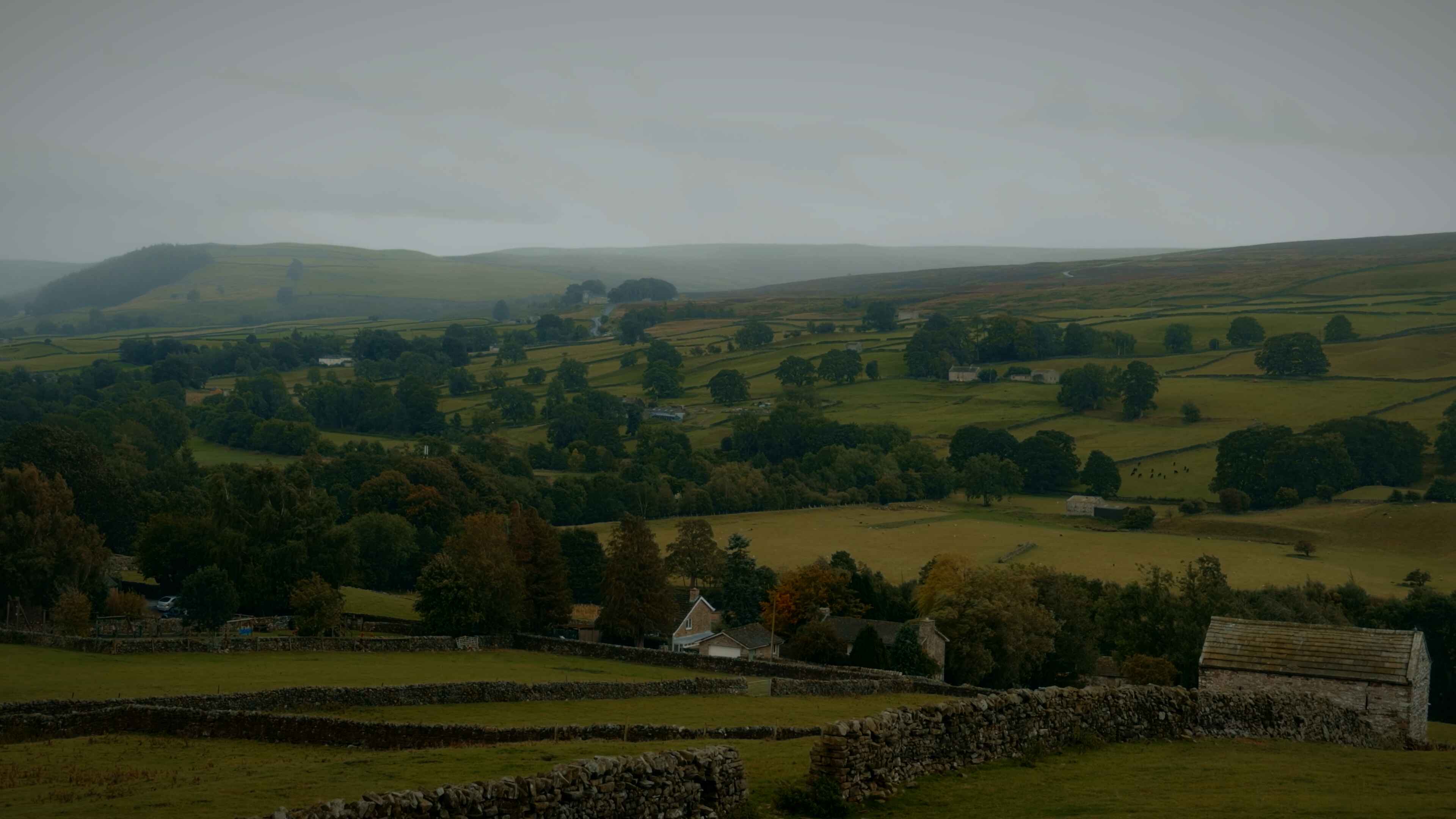 A scenic view of fields, hills, forestry and stone-build walls with houses in the distance