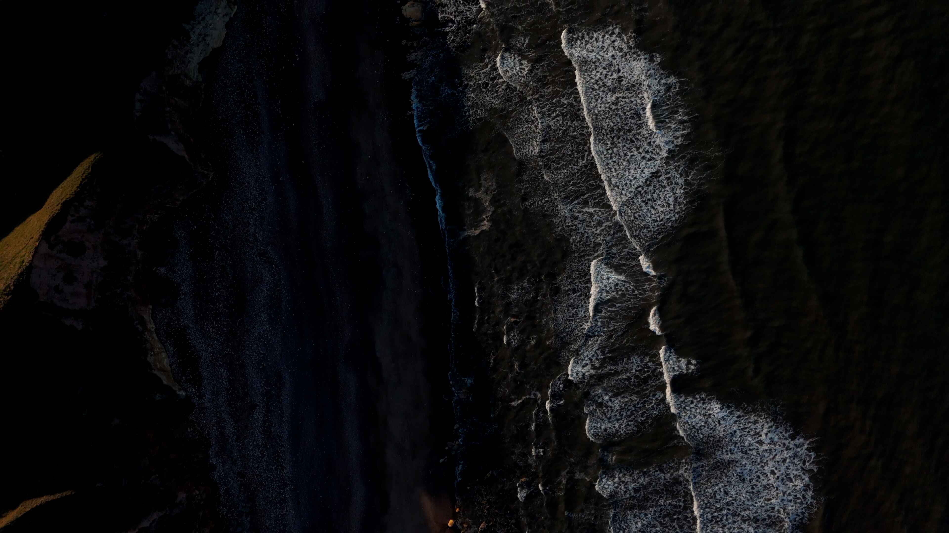 A series of waves overlap the shoreline of a black-sanded beach