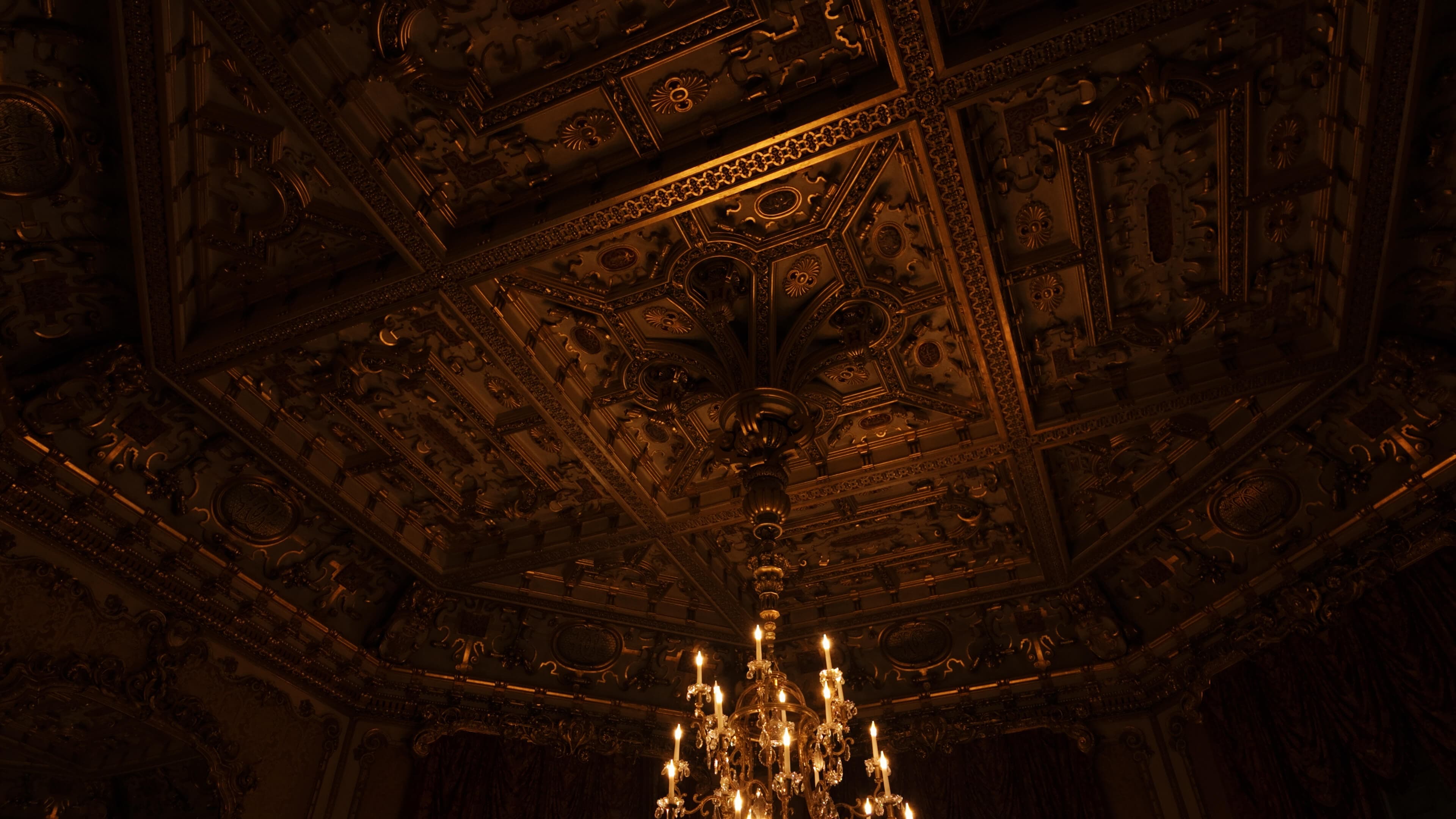 A chandelier glows brightly in a room featuring an intricately designed ceiling