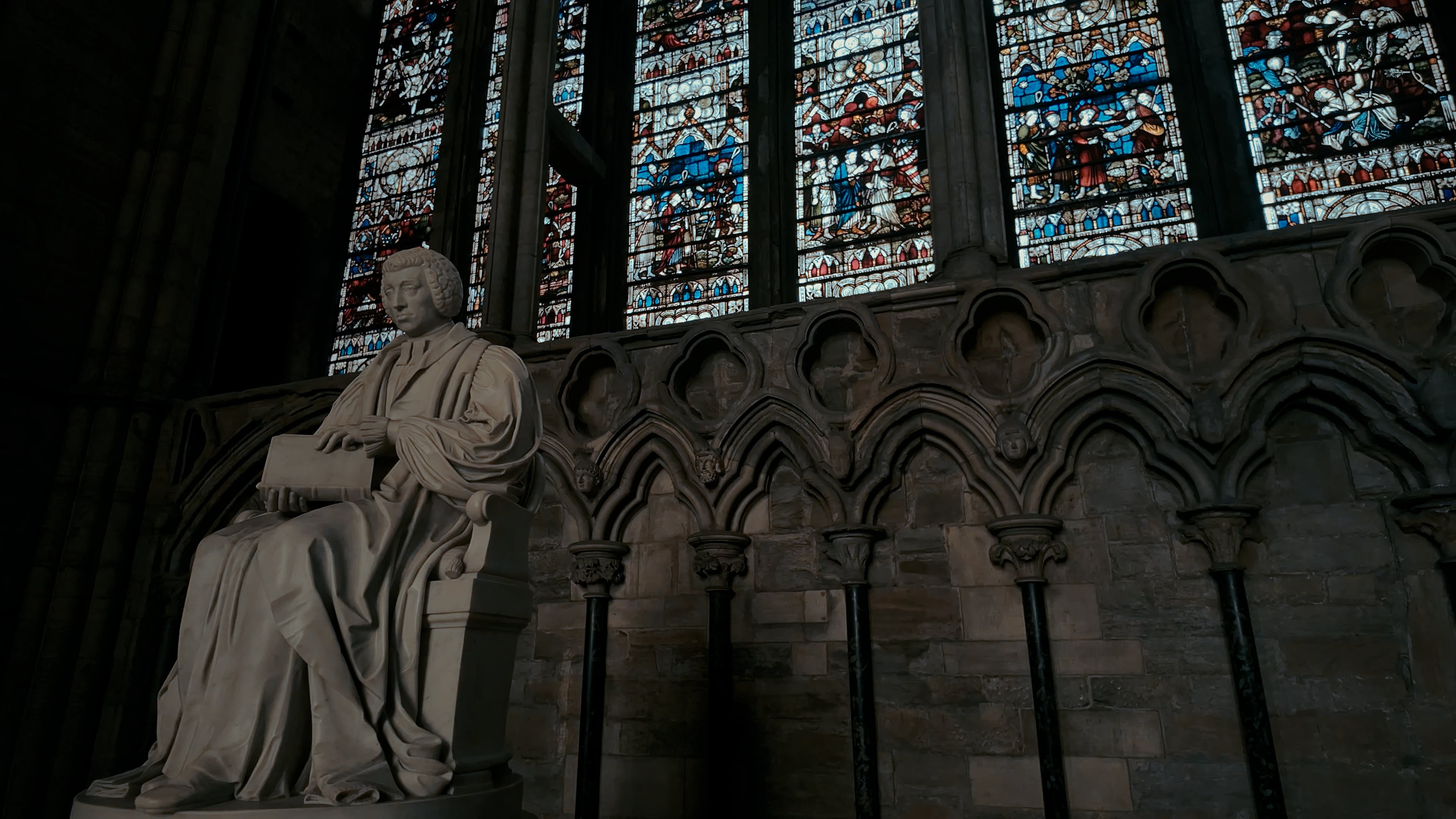 A stained glass window with a statue of a man holding a book in the front