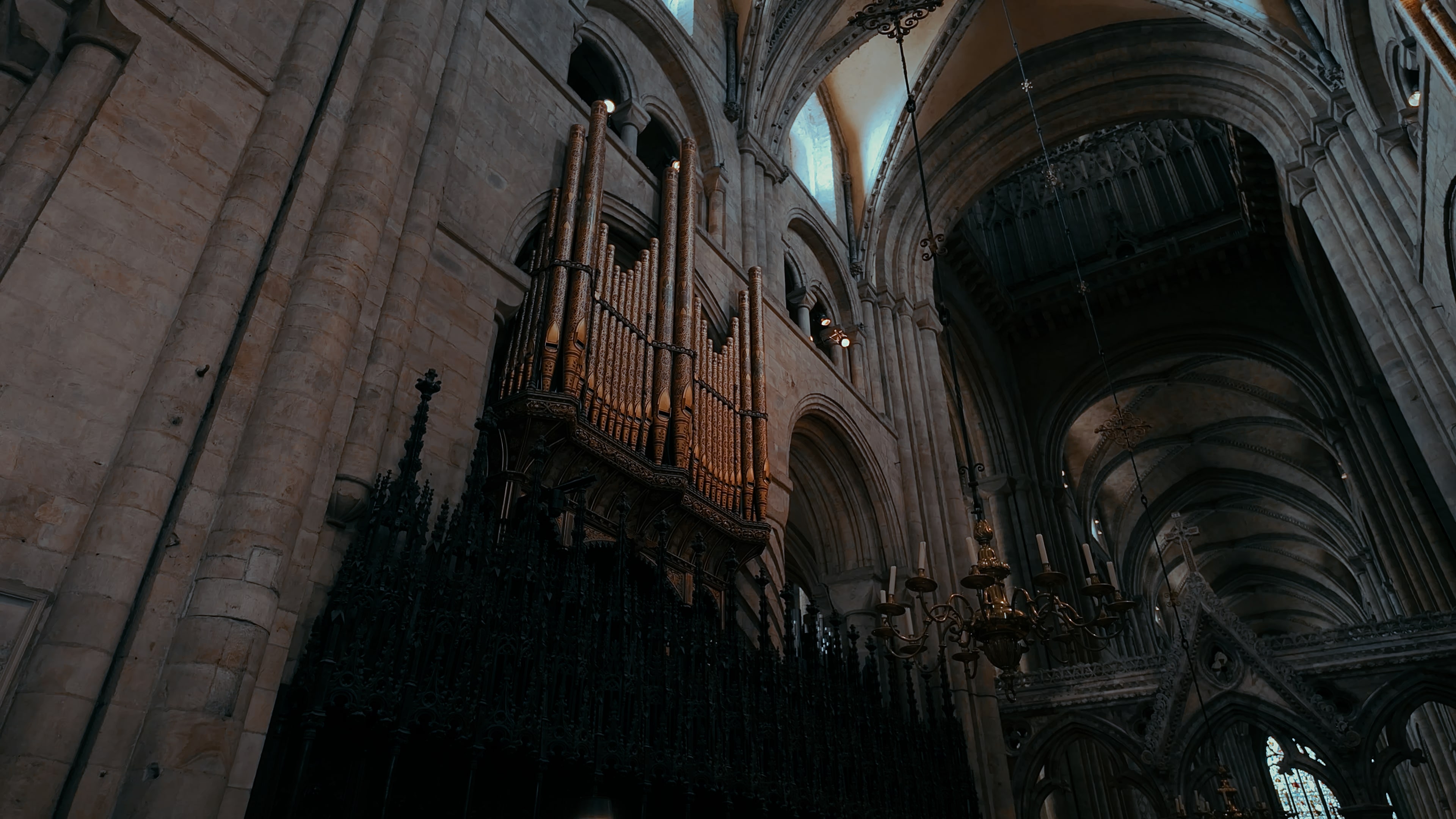 Organ pipes on the left of a cathedral wall and a hanging series of candles upon a chandelier