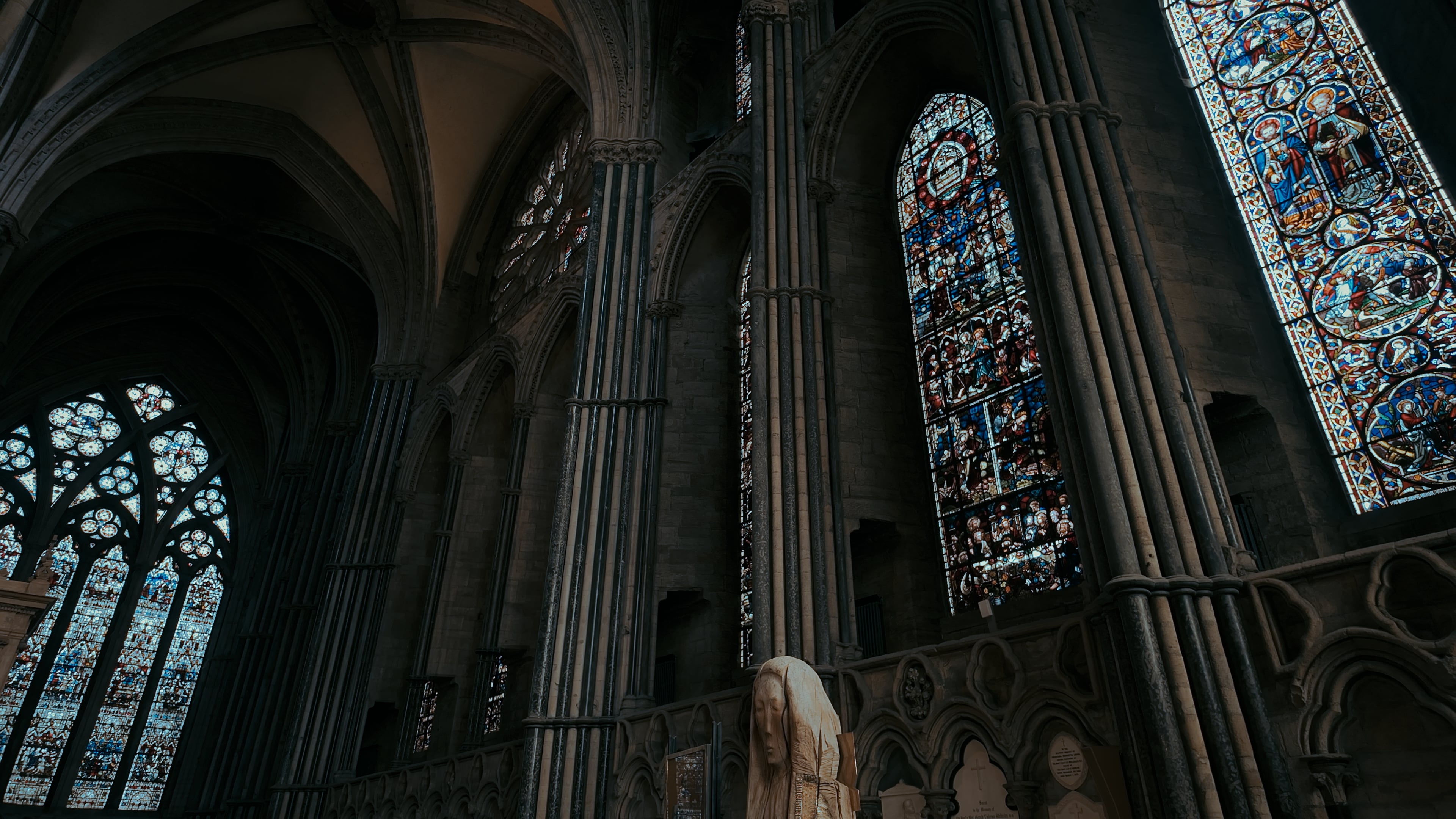 A series of stained glass windows between pillars along a large stretch of cathedral wall