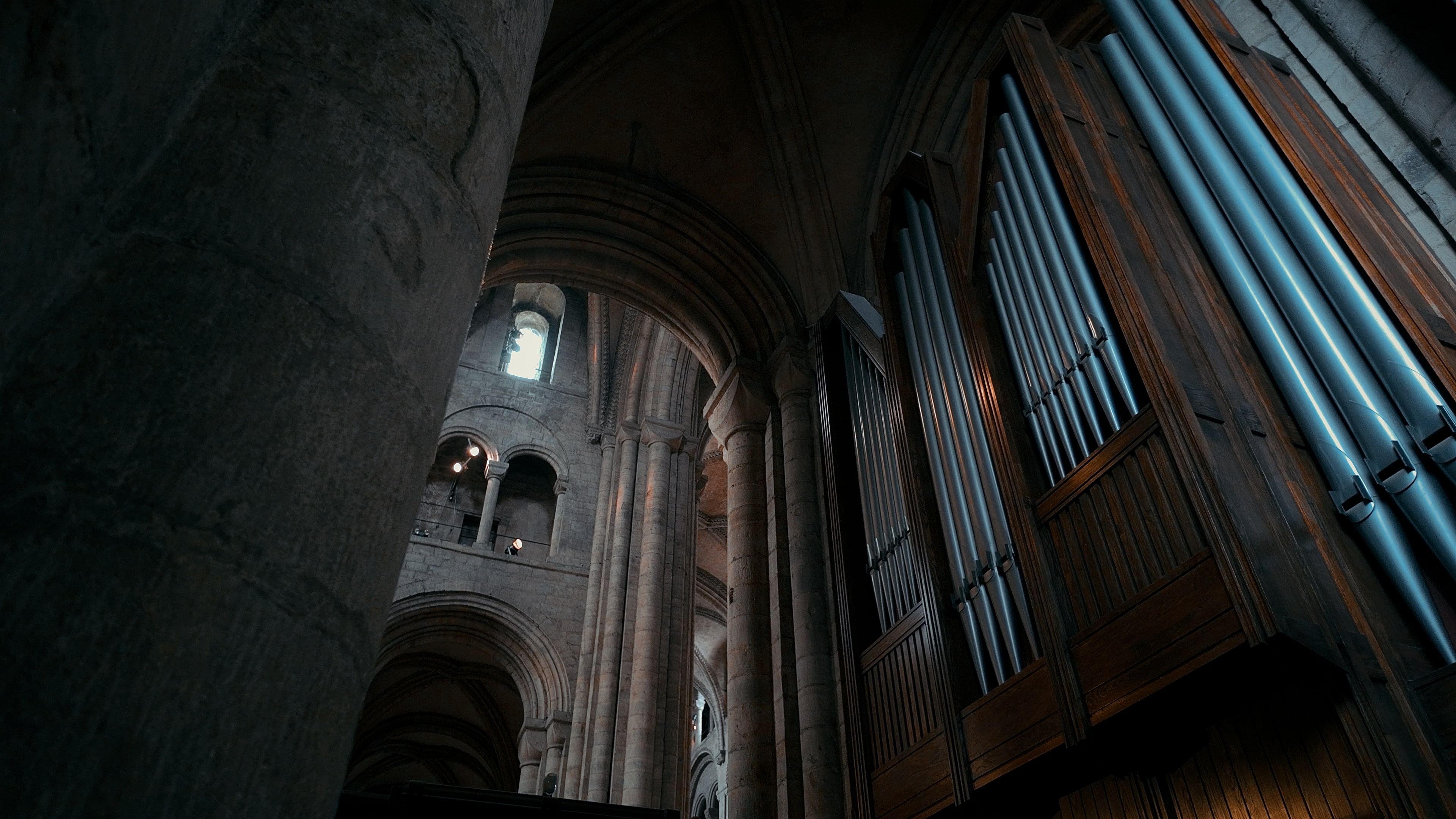 Tall organ pipes inside wooden structures to the right of a cathedral hallway