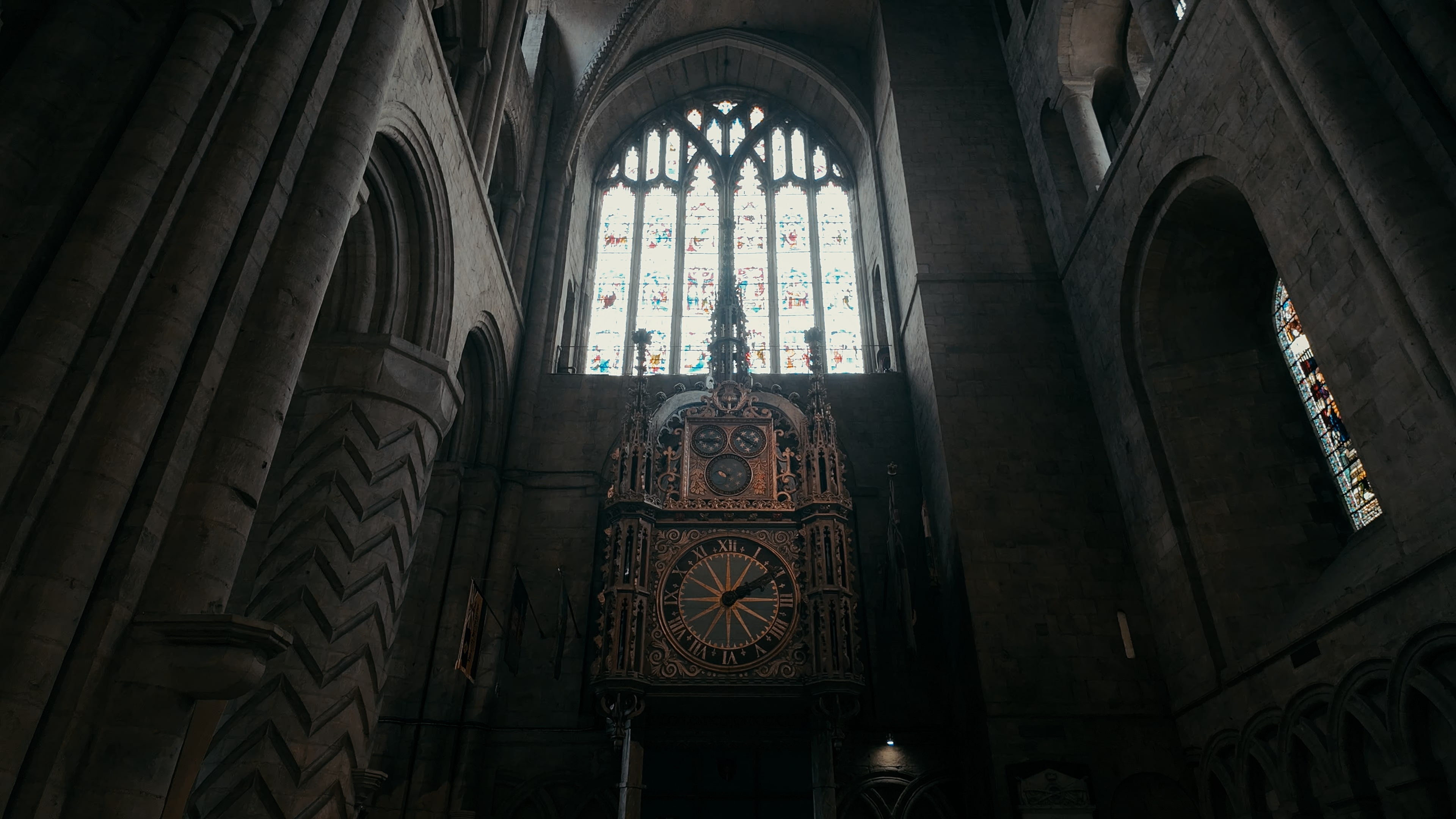 A stained glass-window with a large ornate clock face in between crested stone archways