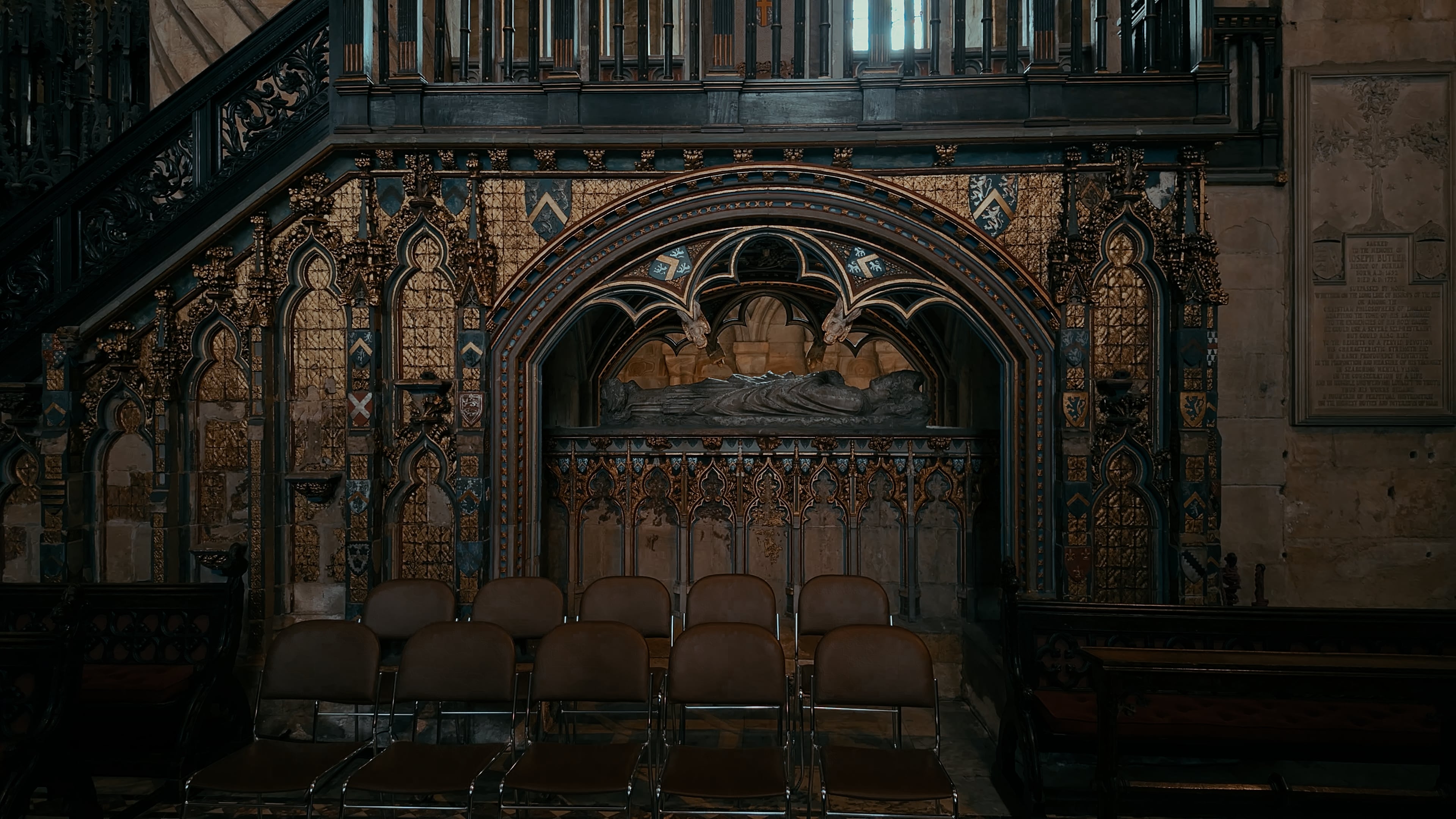 A church tomb underneath a staircase with a series of chairs in front