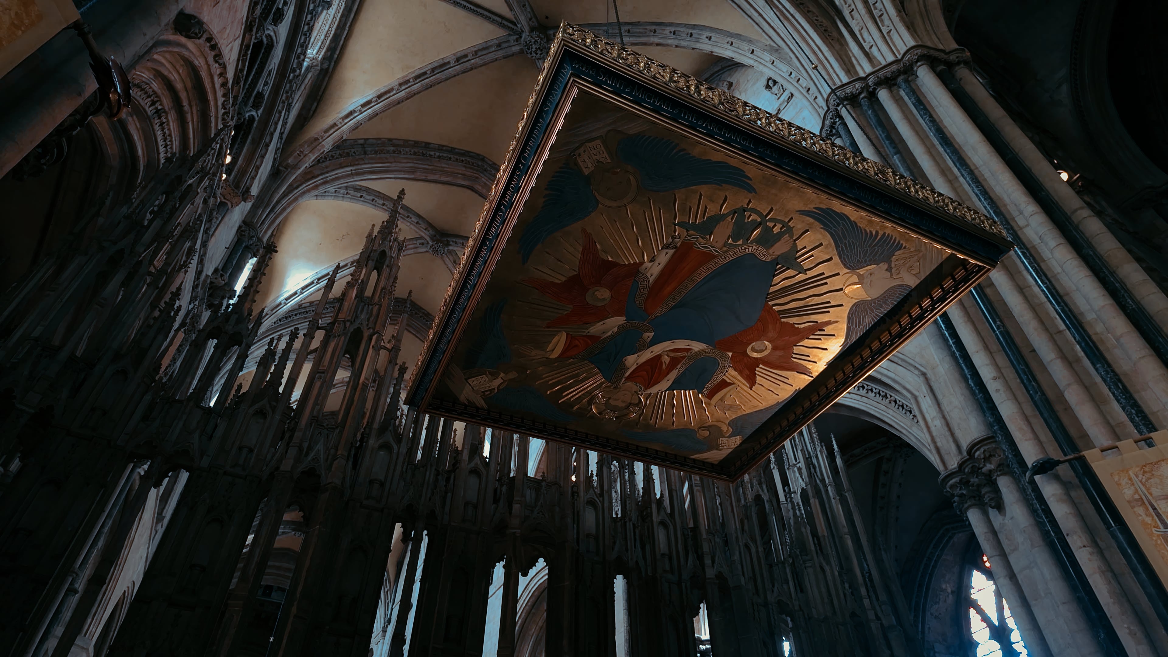 A golden portrait suspended from a ceiling with church spires behind