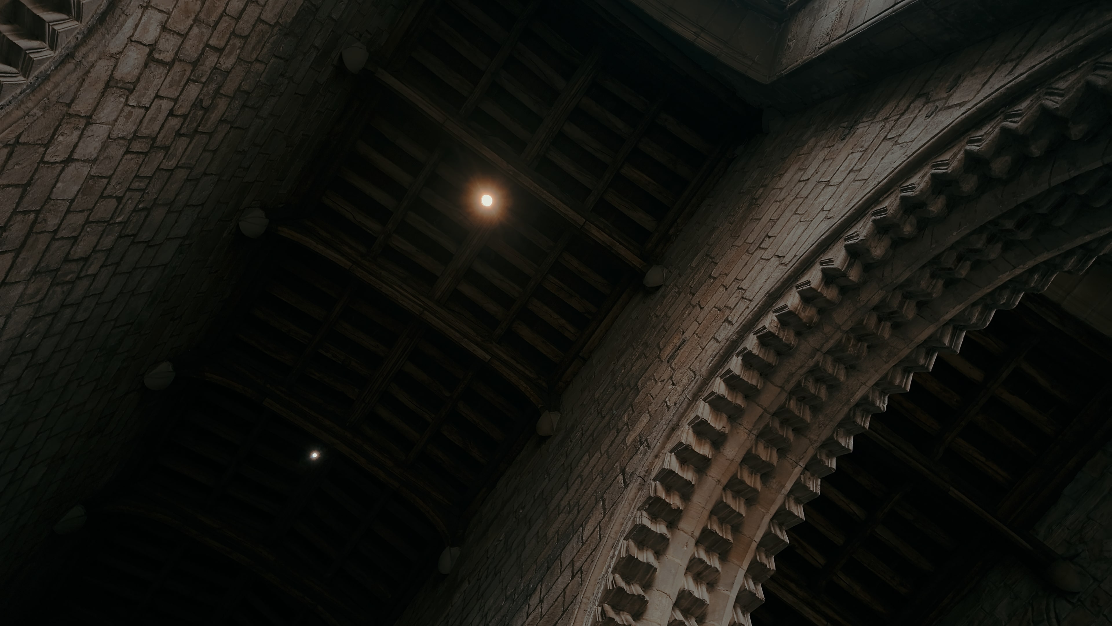 Two lights in the ceiling rafters with stoned curved hallways