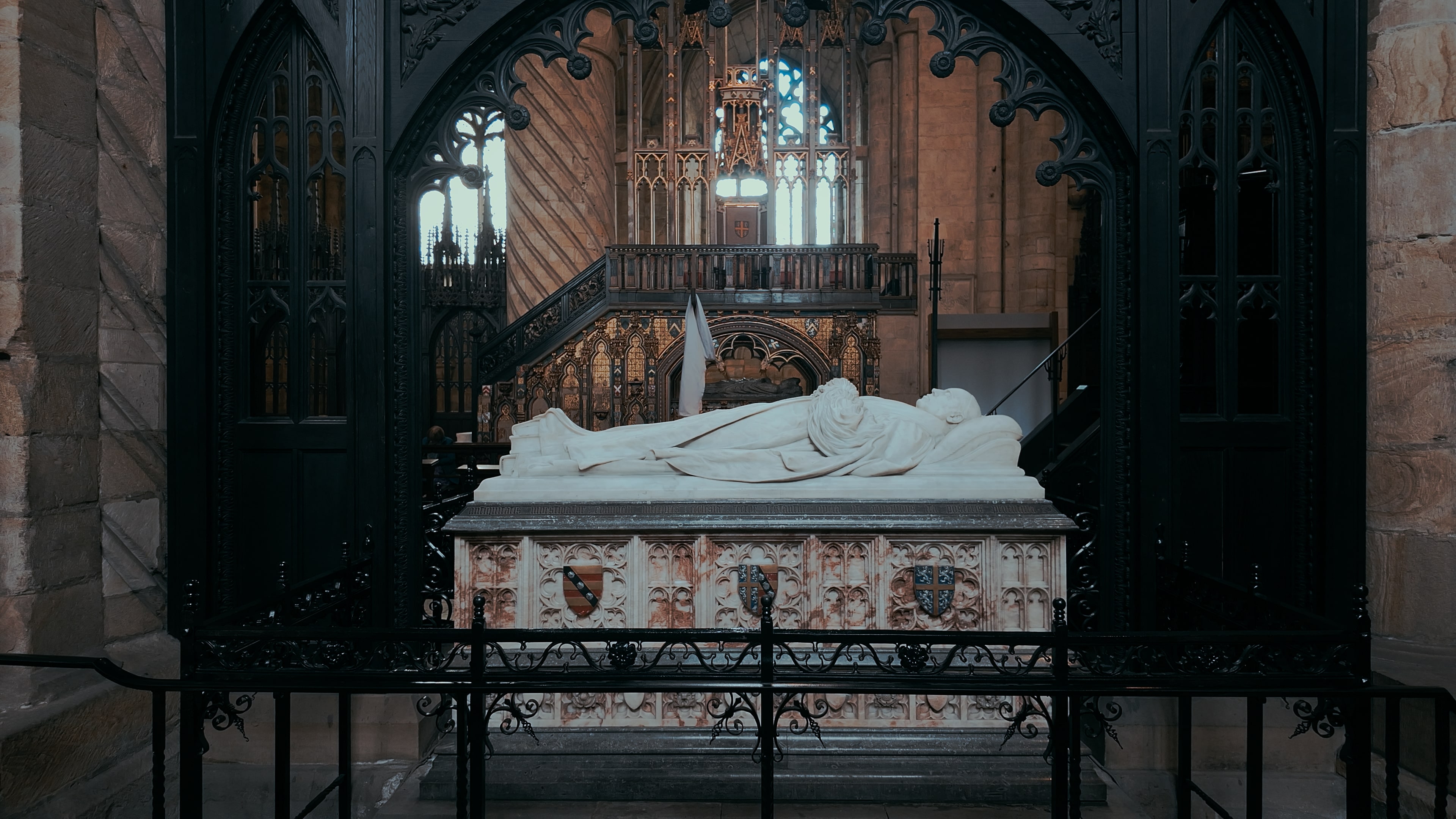 A tomb under a black archway with insignias and a suspended chandelier overhead