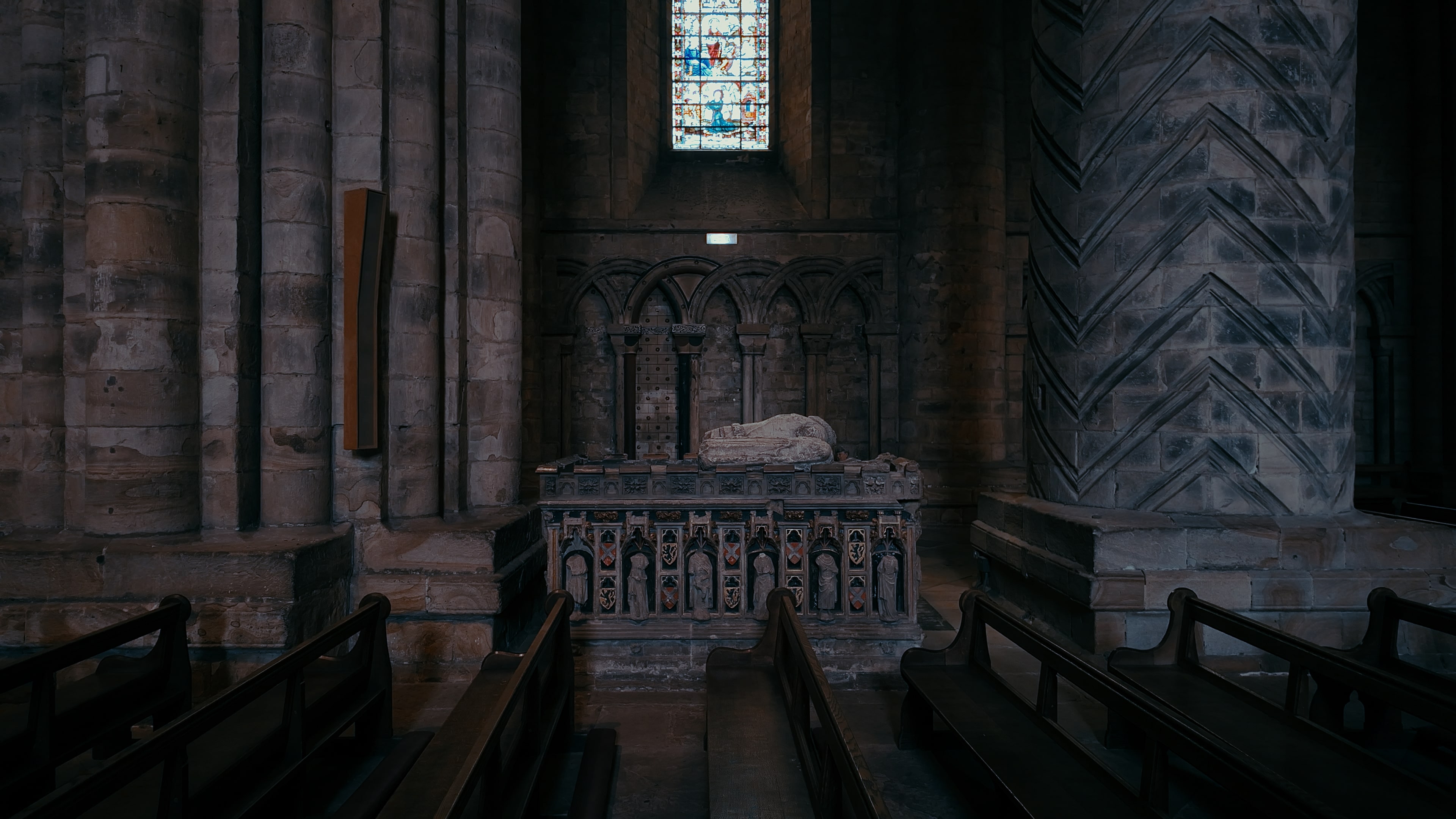 A church tomb in between cathedral pillars with rows of church pews in front