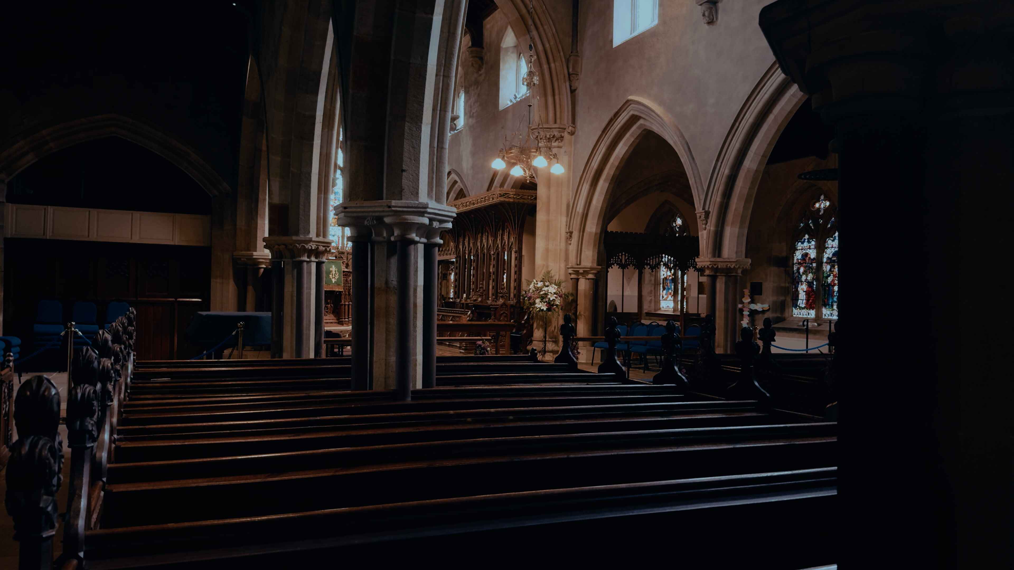 Church pews and arches overhead with suspended lights and blue furnishings